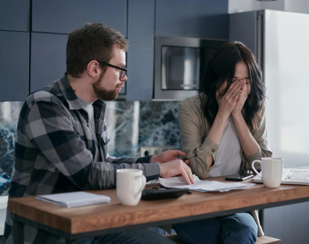 Young couple stresses over bills at home, illustrating financial struggle.